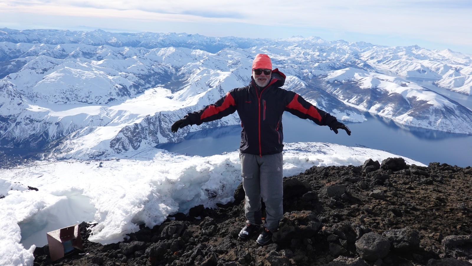 Didier au sommet bravant le fort vent avec en bas à gauche la station de ski de Chacay, le point de départ et au loin les volcans Nevado, Chillan Nuevo et Viejo